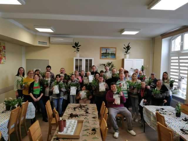 Grupa uczestników biorących udział w akcji sadzenia roślin z dyplomami i gotową sadzonką